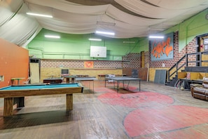 Una sala de billar con mesas, una mesa de billar y una pared de ladrillo con grafitis.