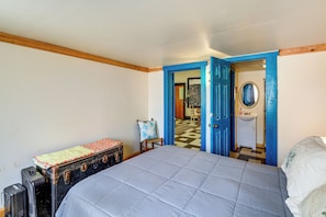 Un dormitorio con cama, maleta, silla y baño visible a través de una puerta abierta.