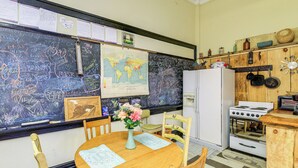 Una cocina con una mesa de madera, sillas, un refrigerador, estufa y una pizarra con anotaciones.