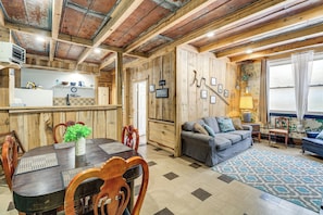 A rustic interior with a wooden dining table, chairs, a sofa, and a patterned rug.