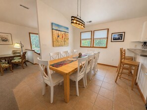 A dining area with a wooden table and white chairs, a hanging light fixture, and artwork on the walls.