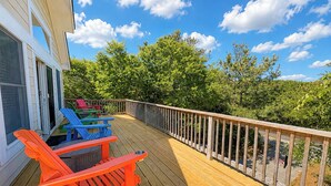 Une terrasse en bois, dotée de meubles d’extérieur, d’une rambarde et offrant une vue sur les arbres et le ciel.