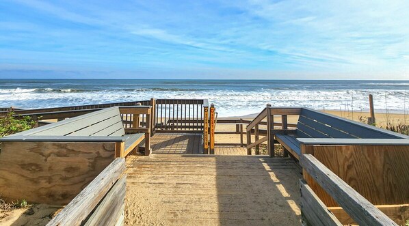 A wooden boardwalk leading to a beach with a bench and a sign.