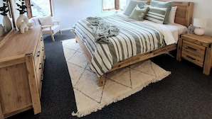 Une chambre à coucher avec un lit, des tables de chevet, une commode, un miroir et des fenêtres.