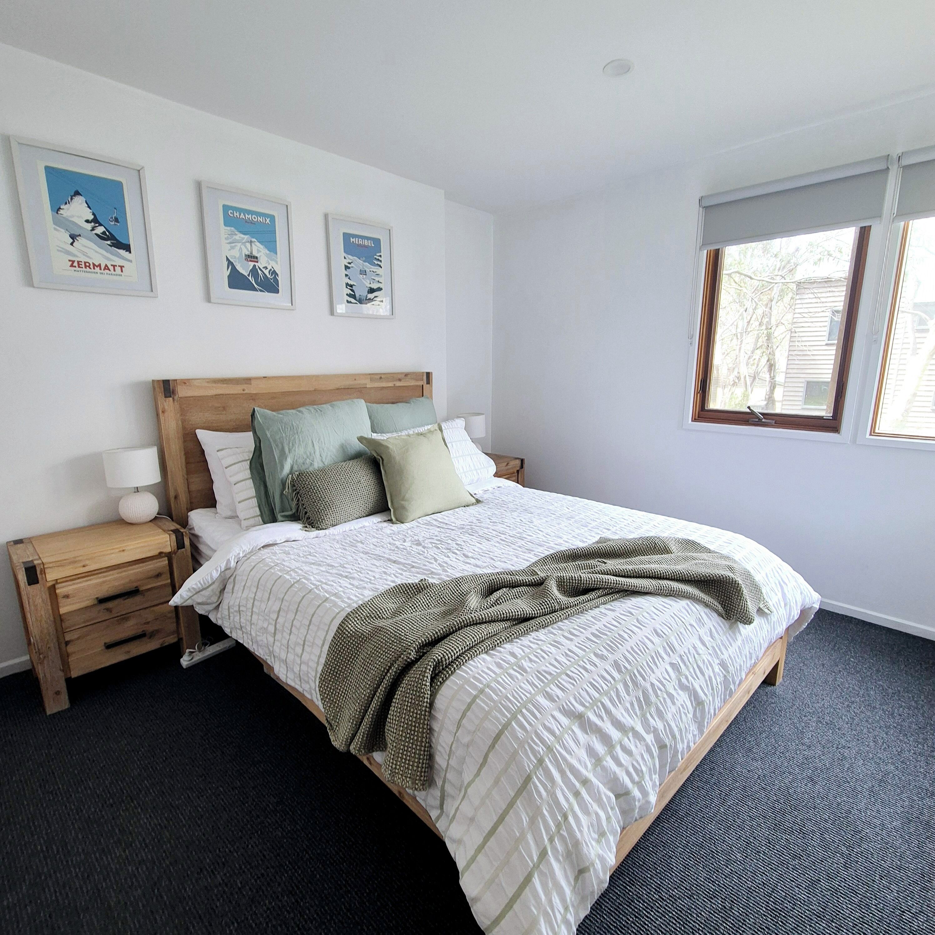 A bedroom with a wooden bed, a nightstand, a window, and three framed pictures on the wall.