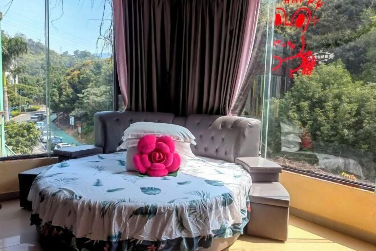 A bedroom with a large window, a bed with a floral bedspread, and a decorative rose.