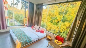 A bedroom with a large bed, a chair, and a view of trees through a window. - Yimu Huatian Inn (Shenzhen)