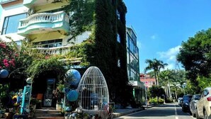 A multi-story building with balconies, a covered entrance, and a street view with parked cars and greenery. - Yimu Huatian Inn (Shenzhen)