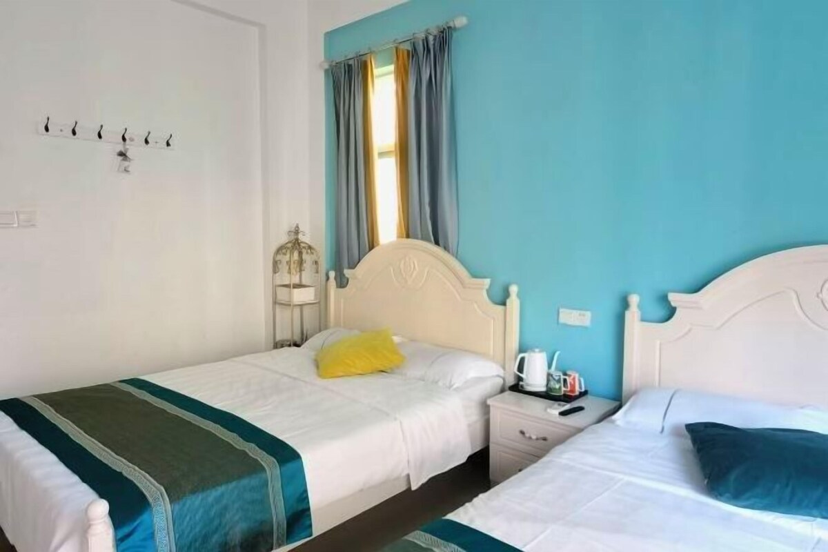 A room with two beds, a window with curtains, a nightstand, and a wall-mounted coat rack.