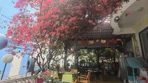 An outdoor cafe area with tables and chairs, a pergola with pink flowers, and a blue building in the background. - Yimu Huatian Inn (Shenzhen)