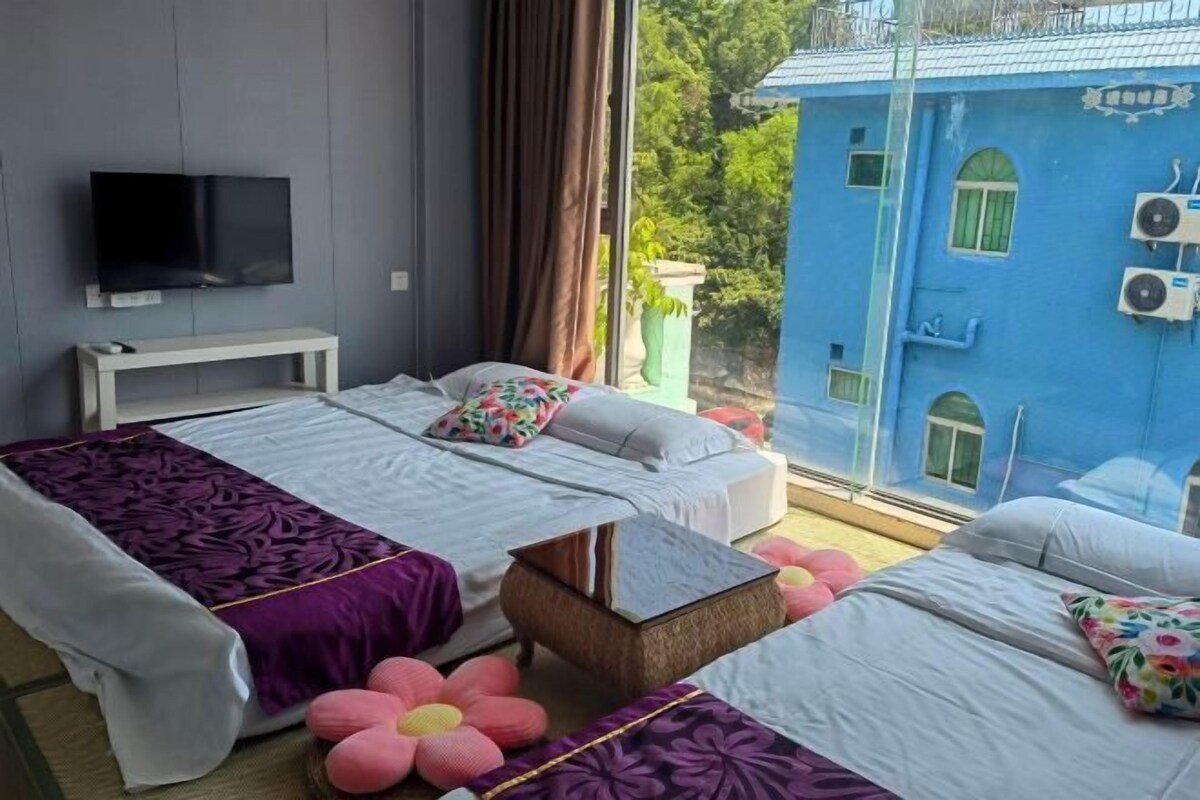 A hotel room with two beds, a TV, and a view of a blue building.