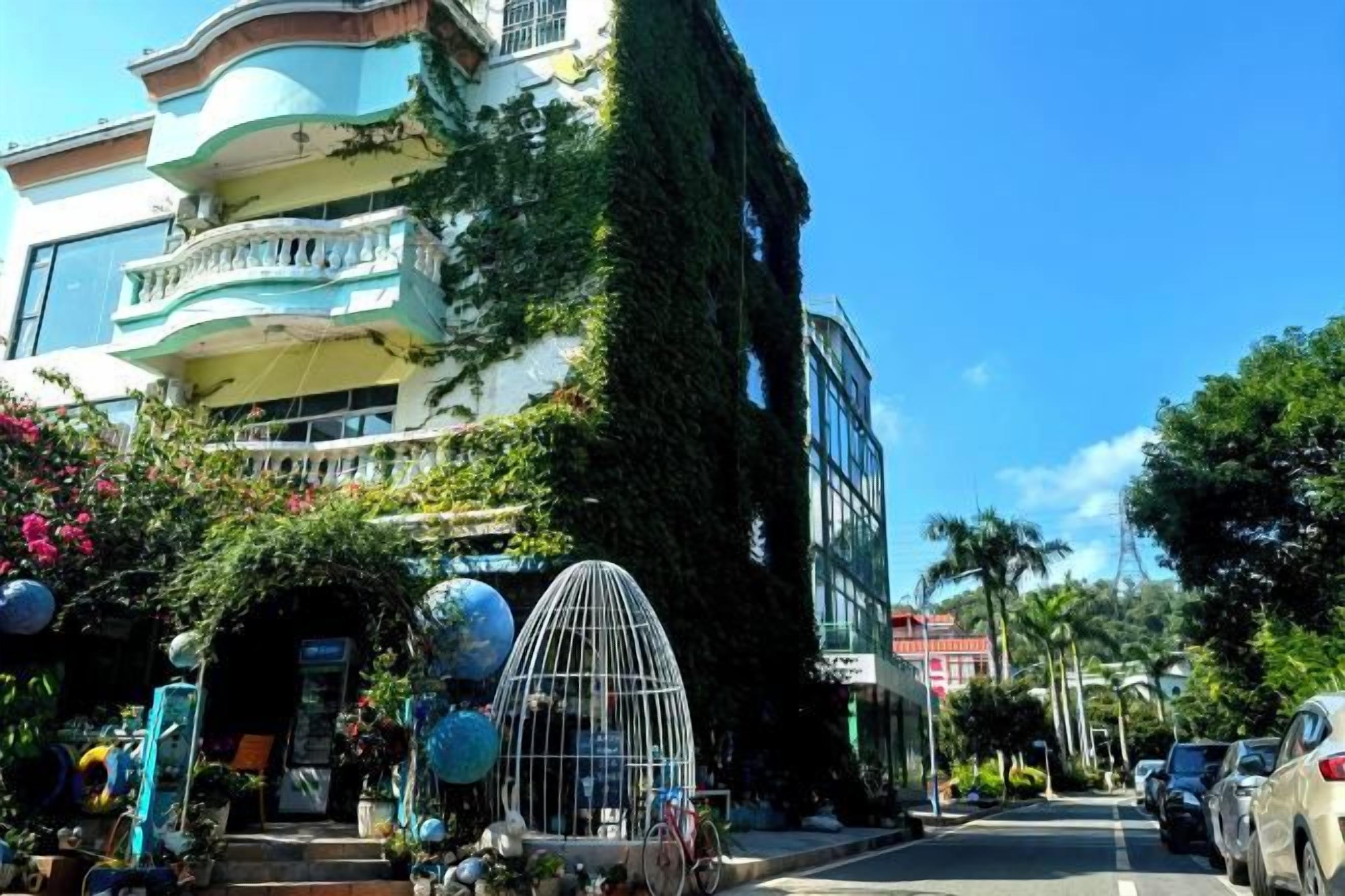 A multi-story building with balconies, a street with parked cars, and a clear sky.