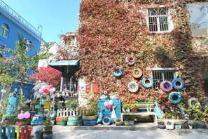 A building covered in ivy with colorful tires hanging on the wall, surrounded by potted plants and flowers. - Yimu Huatian Inn (Shenzhen)