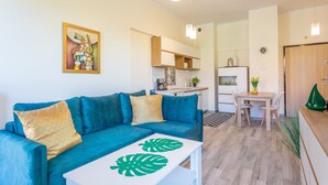 A modern living room with a teal sofa, a white coffee table with a leaf design, a kitchen in the background, and pendant lighting. - Vacation apartment by the sea, vacation on the island of Usedom, Apartment TOWER 22 (Swinoujscie)