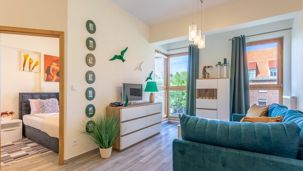 A modern living room with a sofa, a TV, a side table, and a bed. There are decorative items on the wall and a window with curtains. - Vacation apartment by the sea, vacation on the island of Usedom, Apartment TOWER 22 (Swinoujscie)