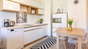 A modern kitchen with white cabinetry, a dishwasher, a coffee maker, and a dining area with a table and chairs. - Vacation apartment by the sea, vacation on the island of Usedom, Apartment TOWER 22 (Swinoujscie)