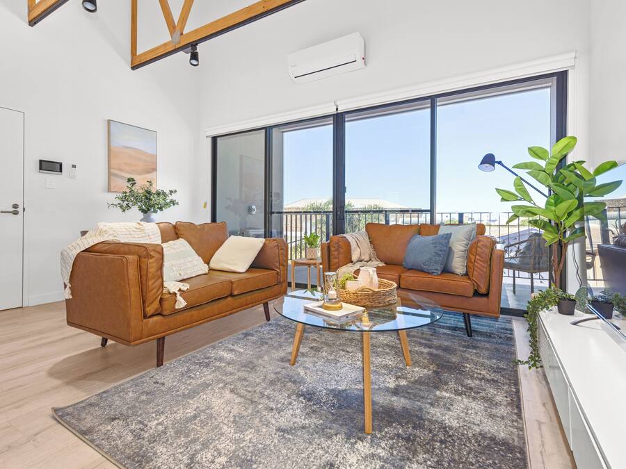Una sala de estar moderna con dos sofás de cuero marrón, una mesa de centro de vidrio y un ventanal con vistas al exterior.