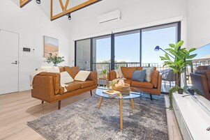Uma sala de estar moderna com dois sofás de couro marrom, uma mesa de centro de vidro e uma grande janela com vista para o exterior.