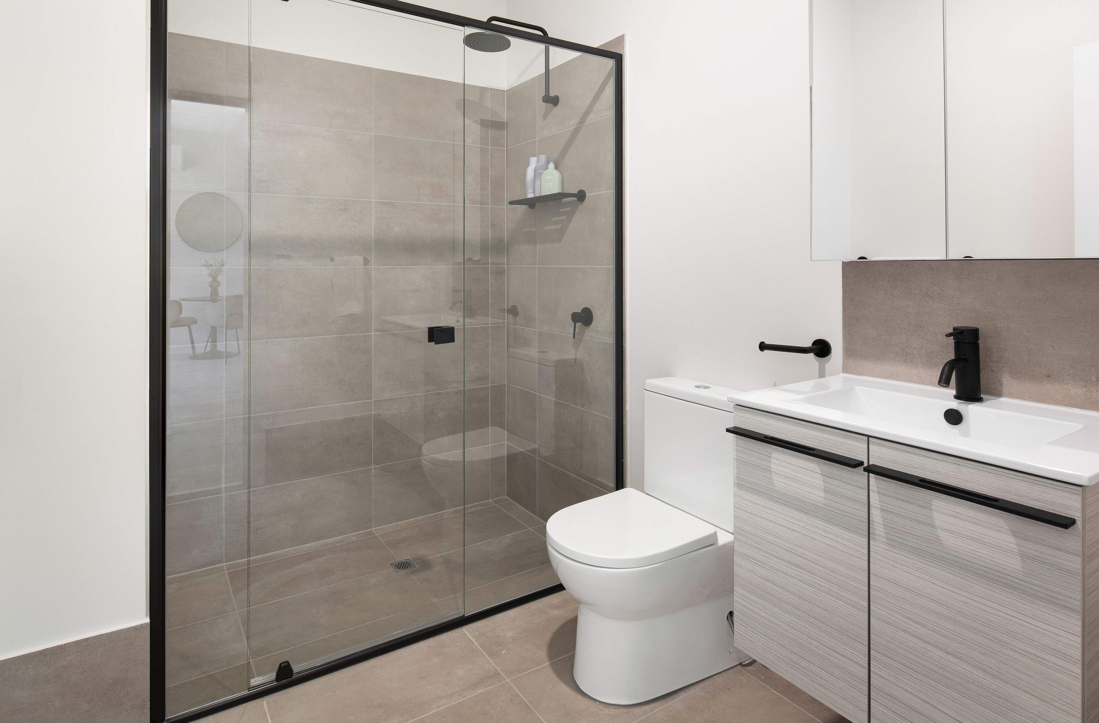 A modern bathroom with a glass-enclosed shower, a white toilet, and a sink with a black faucet.