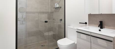 A modern bathroom with a glass-enclosed shower, a white toilet, and a sink with a black faucet.