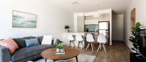 A modern living room with a grey sofa, a coffee table, and a dining area with white chairs.