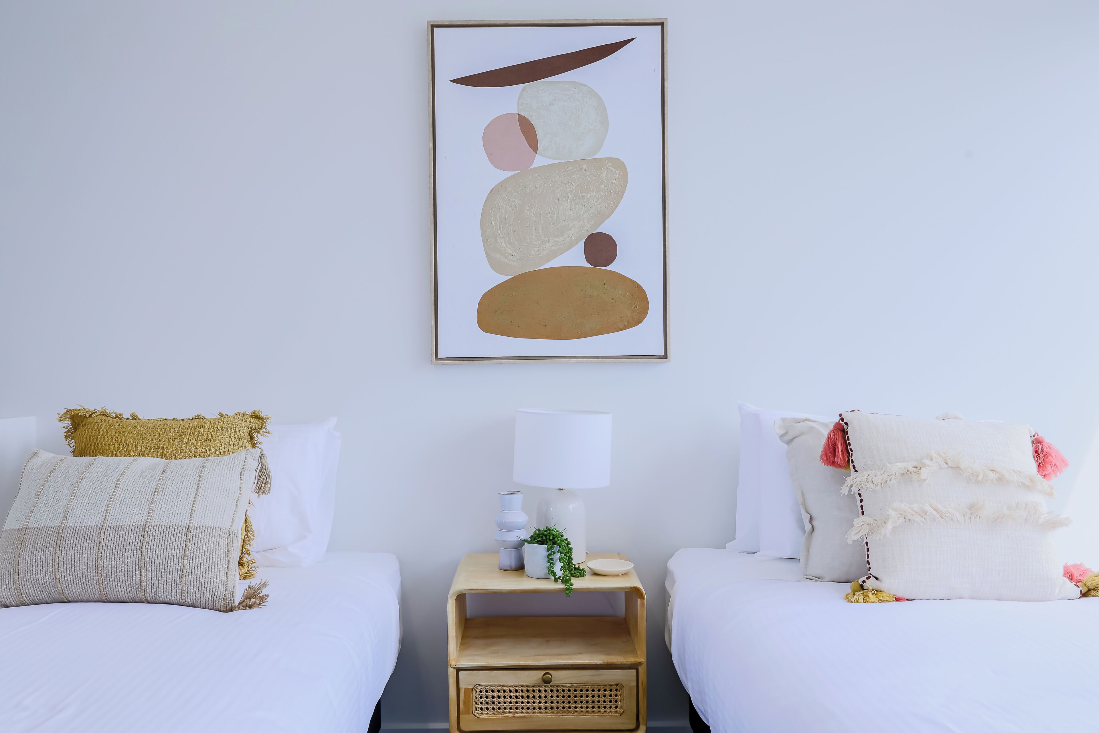 A hotel room with two beds, a bedside table with a lamp, and a wall-mounted abstract art piece.