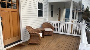 A wooden deck with two wicker chairs and a small table, white railings, and a garage door. - Airy Downtown 1BR w/ Parking (Princeton)