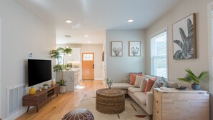 A modern living room with a flat-screen TV, a sofa, a coffee table, and a dining area in the background. - Airy Downtown 1BR w/ Parking (Princeton)