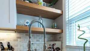 A kitchen with a stainless steel sink, wooden shelves, and a window with blinds. - Airy Downtown 1BR w/ Parking (Princeton)