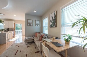 Relax in a stylish living space with a sofa, dining table, and kitchen area, surrounded by artwork and lush greenery.