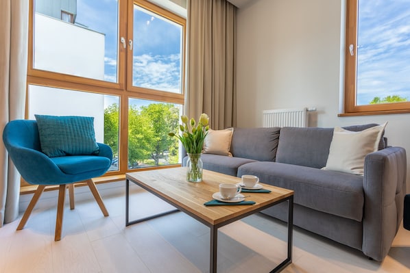 A modern living room with a blue chair, grey sofa, and a wooden coffee table with two cups.