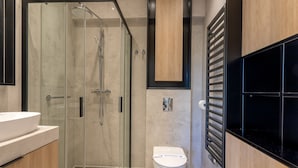 Un baño moderno con ducha de vidrio, inodoro blanco y tocador de madera.