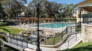 Una piscina con bordo in pietra, una pergola in legno e una scala in pietra che conduce a una zona coperta.