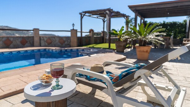 A poolside setting with a lounge chair, a table with snacks and a drink, and a pergola in the background. - Torrox 006 (Torrox)