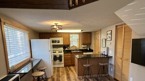 A modern kitchen with wooden cabinets, a white refrigerator, a stove, and a bar area with stools. - Moose Landing Cabin C87 with all the amenities (Wasilla)