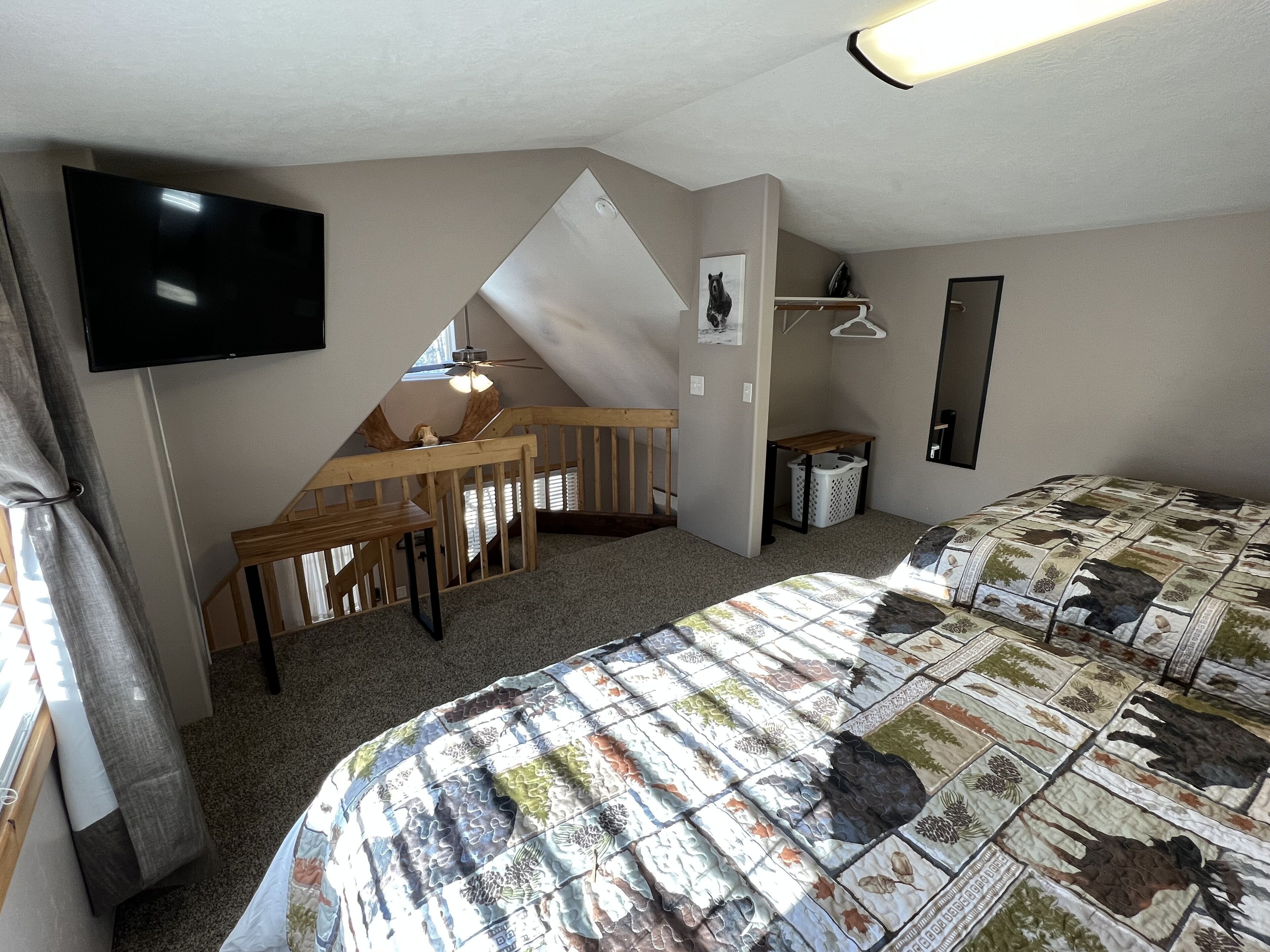 A bedroom with a bed, a desk, a chair, a television, a mirror, and a ceiling fan.