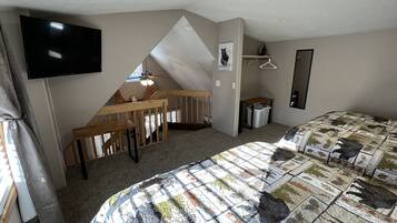 A bedroom with a bed, a desk, a chair, a television, a mirror, and a ceiling fan.