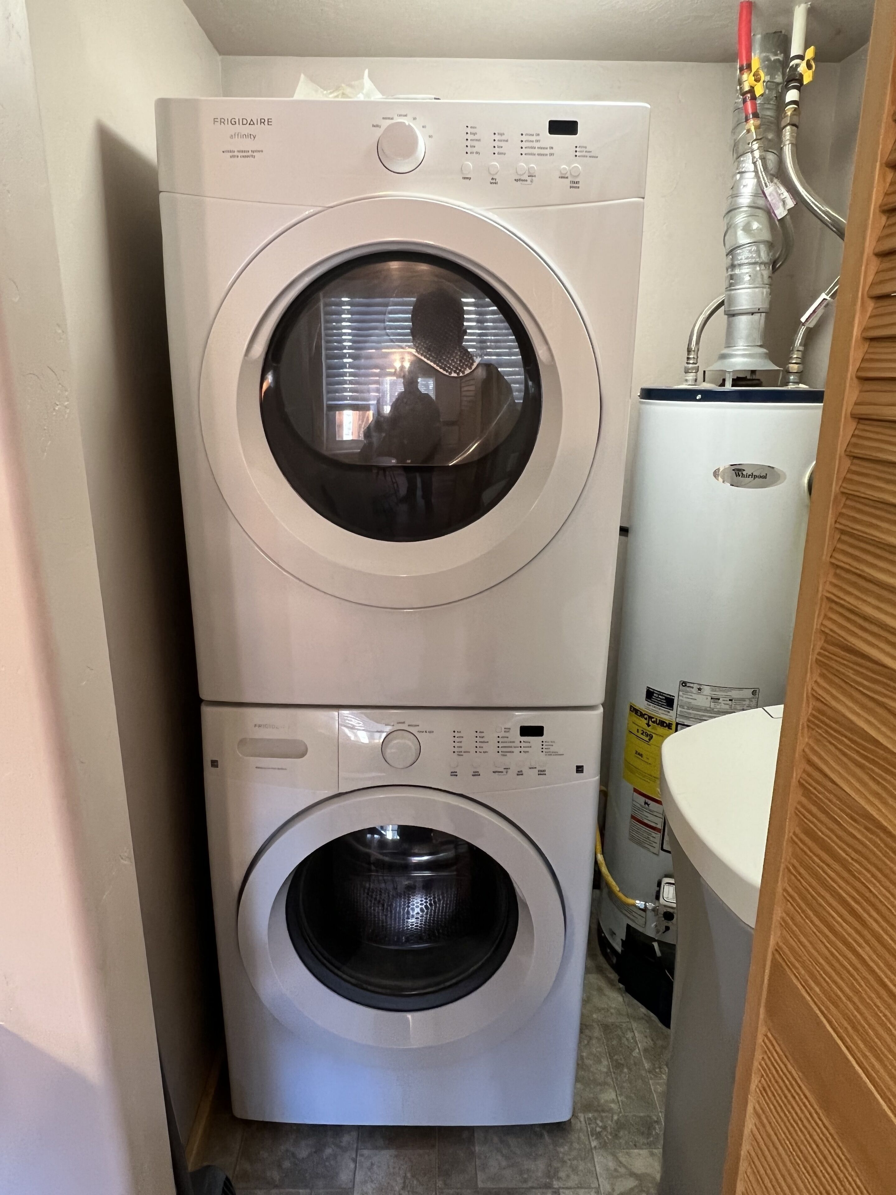 Un appareil combiné lave-linge et sèche-linge, avec un panneau de commande, le reflet visible d’une personne, et une étiquette de la marque Whirlpool.