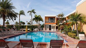 A pool area with lounge chairs, a building with a balcony, and palm trees. - Satellite Motel - The Hideaway 125 (Treasure Island)