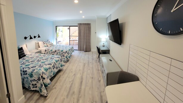 A hotel room with a bed, a desk, a chair, a TV, and a clock. - Satellite Motel - The Hideaway 125 (Treasure Island)