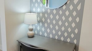 A small desk with a lamp and a mirror, set against a wall with a geometric pattern. - Satellite Motel - The Hideaway 125 (Treasure Island)