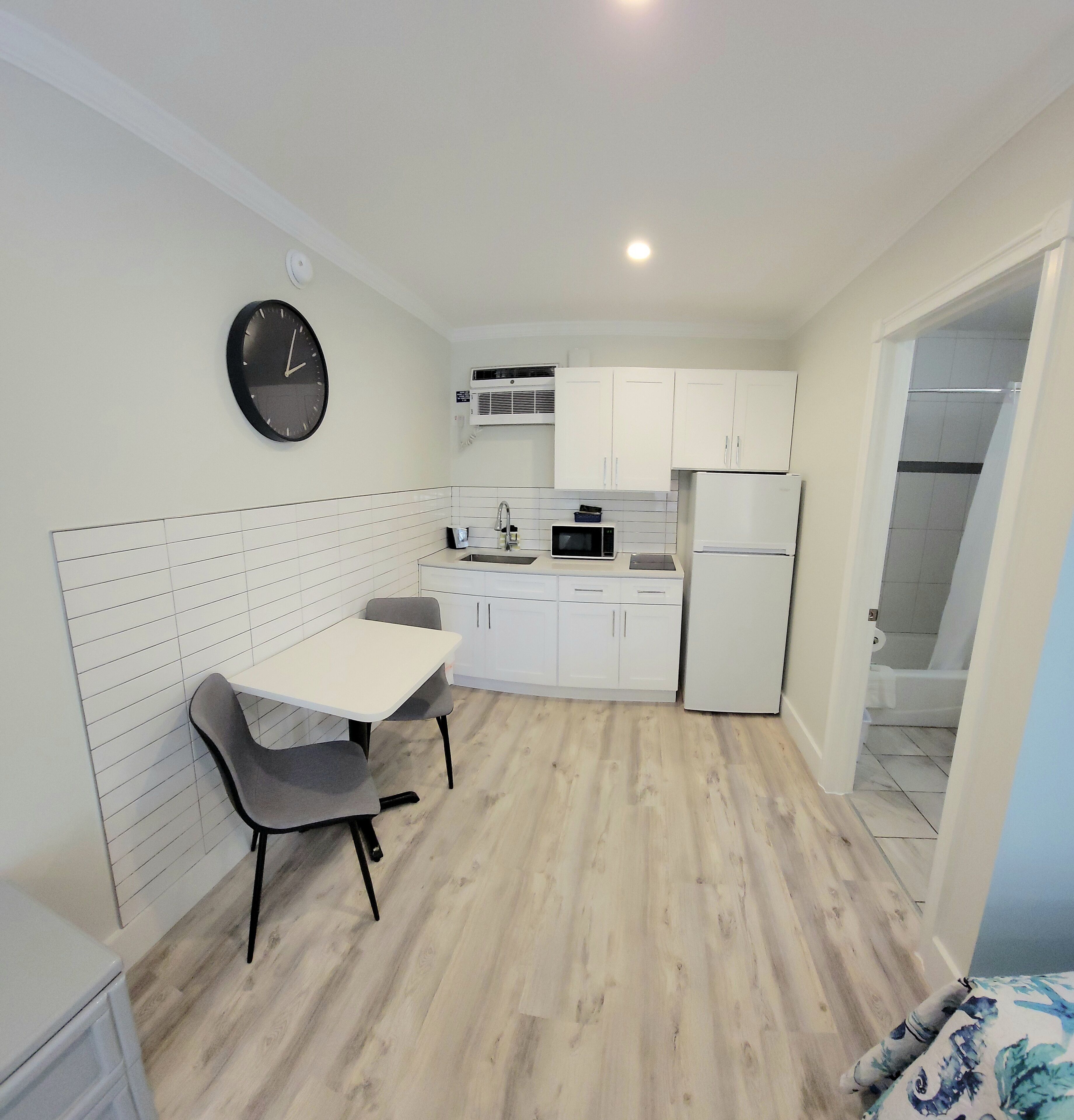 A compact kitchen with white cabinets, a microwave, a refrigerator, and a dining area with a table and chairs.