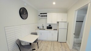 A compact kitchen with white cabinets, a microwave, a refrigerator, and a dining area with a table and chairs. - Satellite Motel - The Hideaway 125 (Treasure Island)