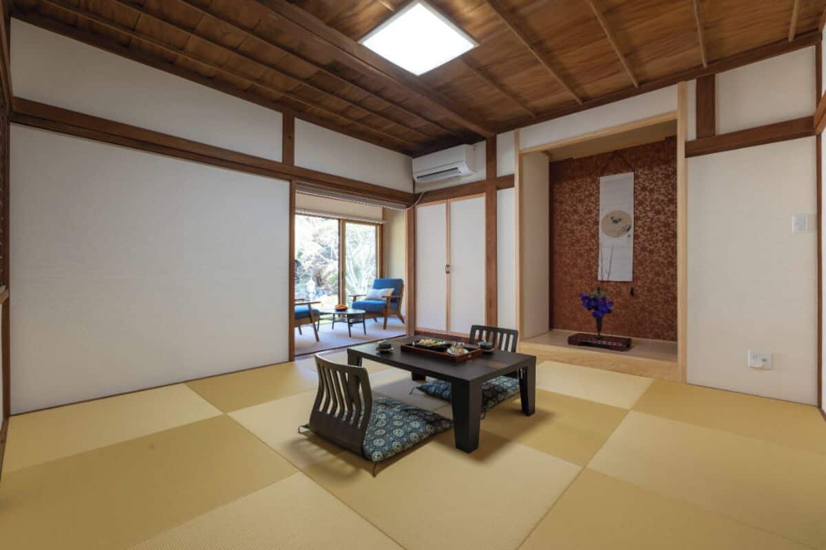 A traditional Japanese room with tatami flooring, a low table with cushions, and a sliding door leading to an outdoor area.