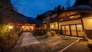 Un bâtiment japonais traditionnel, avec une structure en bois, une lanterne en pierre et un chemin menant à l’entrée.