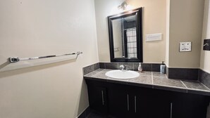 Ein Badezimmer mit einem weißen Waschbecken, dunkelbraunen Schränken, einem Spiegel und einer Haltestange.