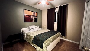 Ein Schlafzimmer mit einem Bett, einem Deckenventilator, einem Fenster mit Vorhängen und einem Bild an der Wand.