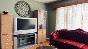 Ein Wohnzimmer mit Flachbildfernseher, Holzschränken, einem roten Sofa und einem Wandbild.
