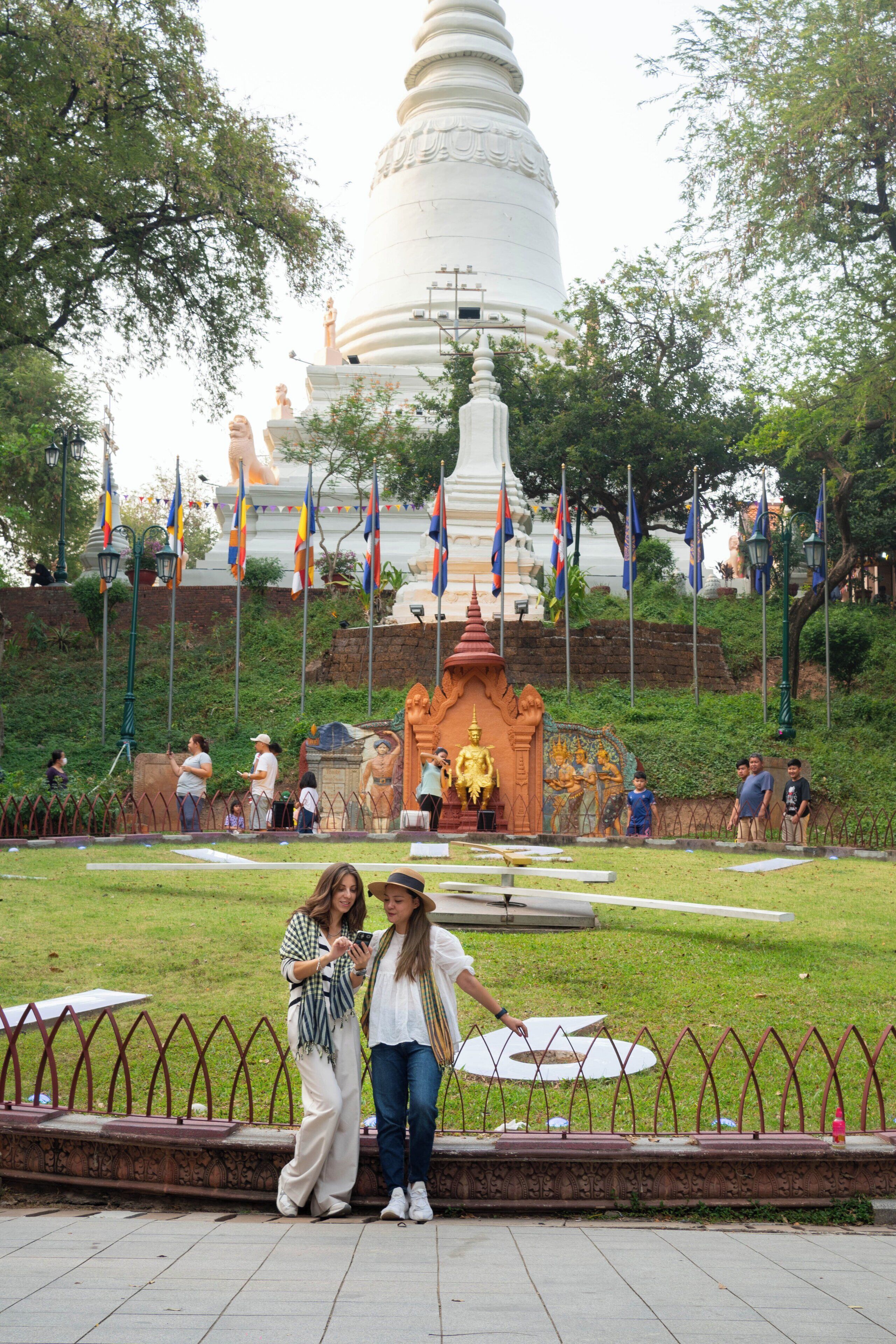 A large white stupa with a golden statue in front, surrounded by flags and a small shrine.