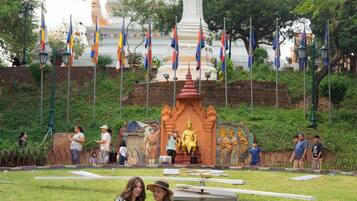 A large white stupa with a golden statue in front, surrounded by flags and a small shrine.